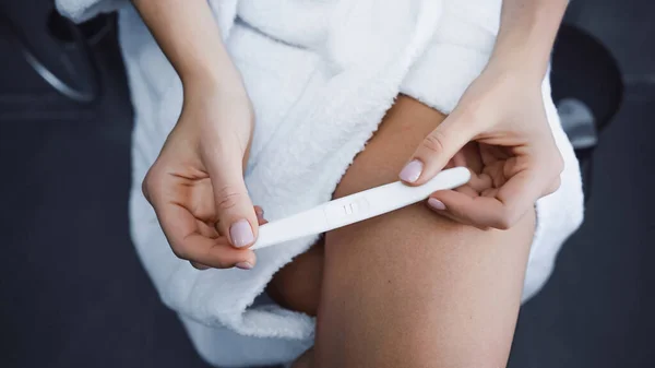 穿着浴衣在浴室里进行怀孕测试的年轻女性的偏视 — 图库照片