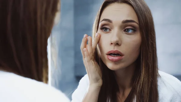 worried woman applying eye cream and looking at mirror