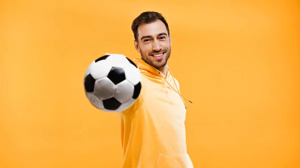 smiling man playing with football isolated on yellow