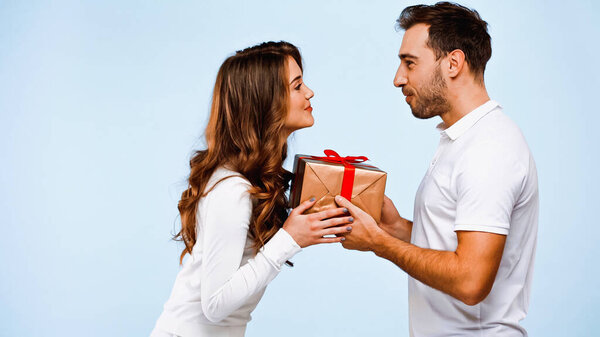 side view of boyfriend giving wrapped present to girlfriend isolated on blue
