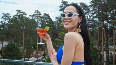 happy brunette woman in sunglasses holding glass of cocktail  clipart