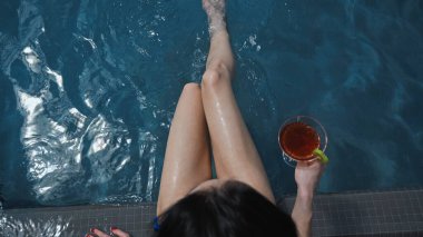 top view of wet woman in swimsuit sitting near pool with cocktail  clipart