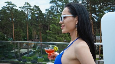 side view of happy brunette woman in sunglasses holding glass with cocktail clipart