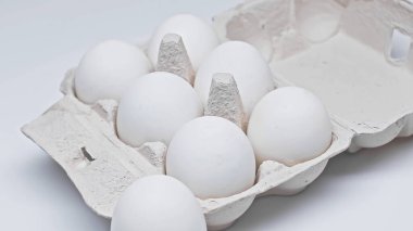 Beyaz yüzeydeki karton kabın içinde taze tavuk yumurtaları.