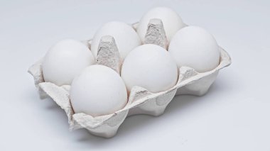 Beyaz yüzeyde karton pakette altı tavuk yumurtası.