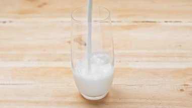 fresh milk pouring into glass on wooden table clipart