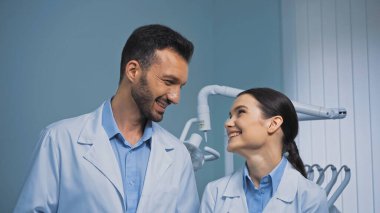 Klinikte birbirine bakan beyaz önlüklü mutlu dişçiler.