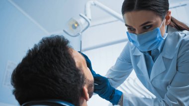 Tıbbi maske takan stomatolog klinikteki hastayı tedavi ediyor.