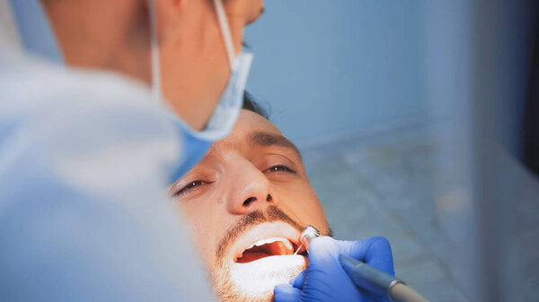 стоматолог в медицинской маске с помощью зубной дрели на пациенте, размытый передний план