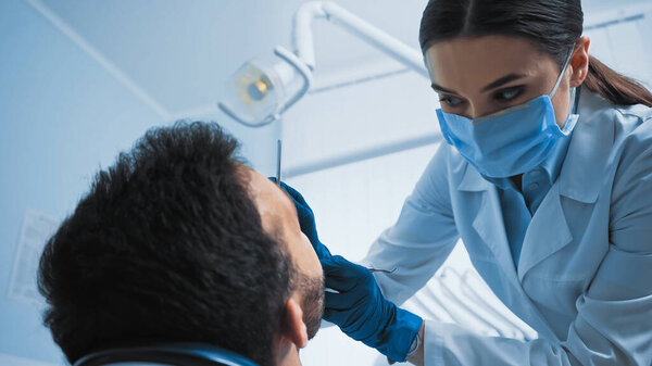 стоматолог в медицинской маске лечит пациента в клинике