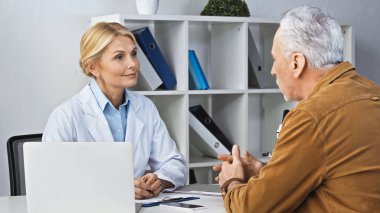 Klinikte danışmanlık yaparken gülümseyen doktorla konuşan olgun bir adam.