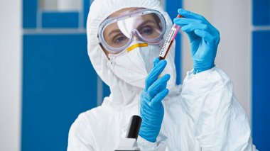 scientist in hazmat suit holding coronavirus test in laboratory clipart