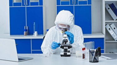 Laboratuvarda mikroskopla çalışan tehlikeli madde giysisi içindeki bilim adamı.