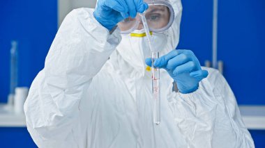 Tehlikeli madde giysisi içindeki virolog laboratuarda deney tüpü ve damlatıcıyı tutuyor.