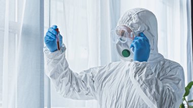 scientist in hazmat suit talking on smartphone while holding test tube with blood sample clipart