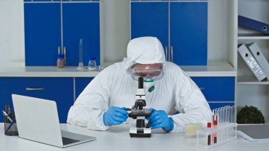 scientist working with microscope near laptop in laboratory clipart