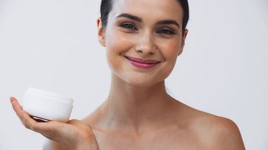 Gri renkte kozmetik krem tutarken kameraya bakan gülümseyen kadın.