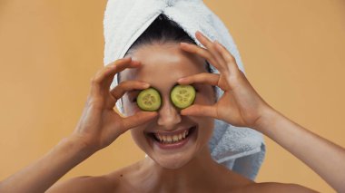 Neşeli kadın, bej üzerine izole edilmiş salatalık dilimleriyle gözlerini kapatıyor.