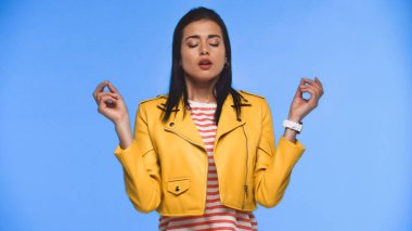 Sarı ceketli genç kadın mavi üzerinde meditasyon yapıyor.