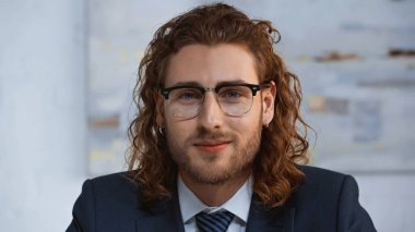 Gözlüklü genç, kıvırcık işadamı ofiste kameraya bakıyor.