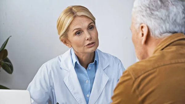 Mature Doctor Talking Patient Appointment Clinic Blurred Foreground — Stock Photo, Image