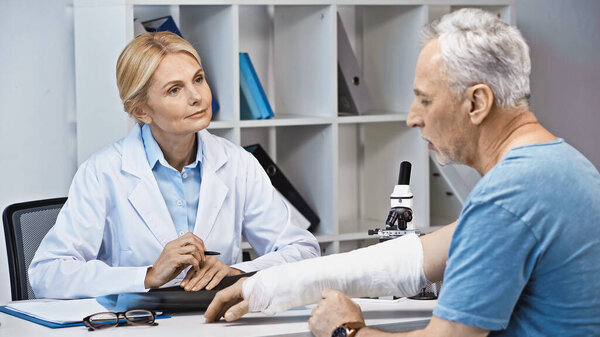  attentive doctor listening to man with broken arm in consulting room