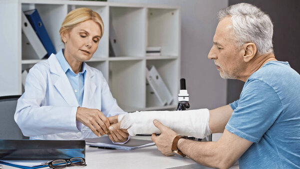 травматолог, осматривающий сломанную руку взрослого мужчины в больнице