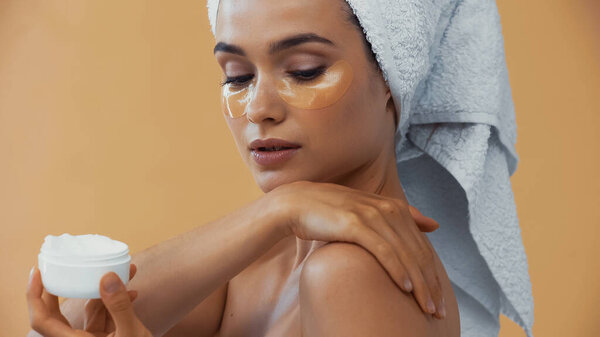 pretty woman with collagen pads under eyes applying body cream isolated on beige