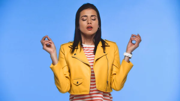 young woman in yellow jacket meditating isolated on blue