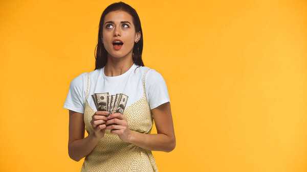 задумчивая молодая женщина держит доллары банкноты изолированы на желтый