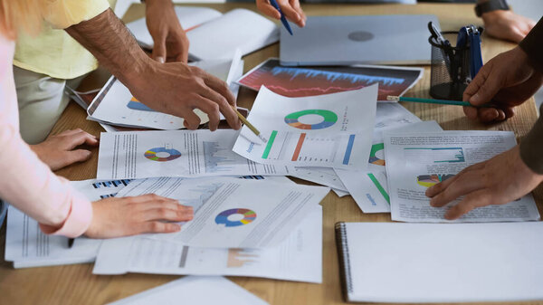 обрезанный взгляд бизнесмена, указывающего карандашом на документ рядом с партнерами на размытом переднем плане