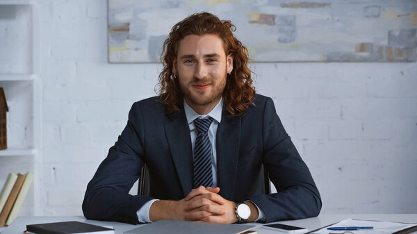 young businessman in suit smiling at camera while sitting at workplace