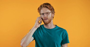 Gözlüklü kızıl saçlı adam sarıda izole edilmiş akıllı telefondan konuşuyor.