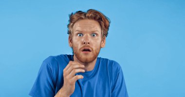 Şok olmuş ve kırmızı tişörtlü adam mavi üzerine izole edilmiş.