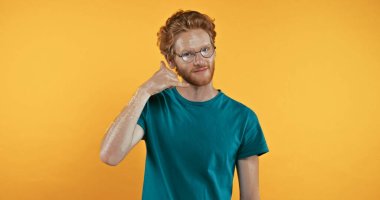 redhead man in t-shirt showing call me gesture isolated on yellow clipart