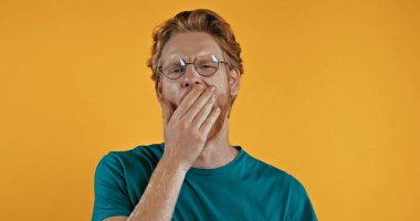 tired redhead man covering mouth isolated on yellow clipart
