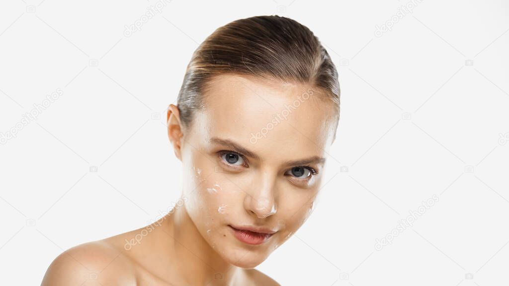 sensual young woman with bare shoulders and cream on face looking at camera isolated on white