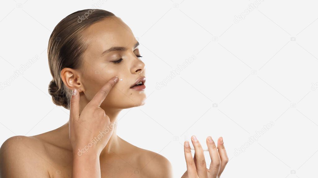 Young woman holding container and applying face cream isolated on white