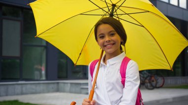 happy schoolgirl with umbrella standing near building clipart