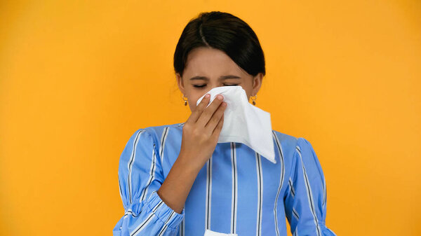 sad sick girl blowing nose with napkin isolated on yellow