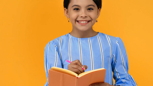 веселая девушка держит карандаш и блокнот изолированы на желтый