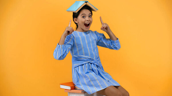 excited kid pointing with fingers at book on head on yellow