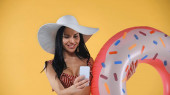 Fröhliche Frau in Badeanzug und Strohhut macht Selfie mit Schwimmring