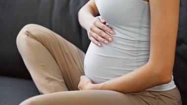 Hamile bir kadının evdeki koltukta karnına dokunduğu görüntüler.
