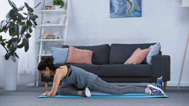 Spor giyimli esnek genç bir kadın evde spor minderinde esniyor. 