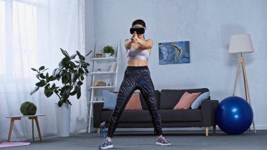 Spor giyimli genç bir kadın ve evde kulaklık takan bir kadın. 