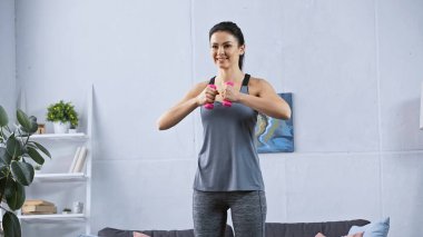 Spor giyim sektöründe genç ve mutlu bir kadın evde dambıllarla çalışıyor. 