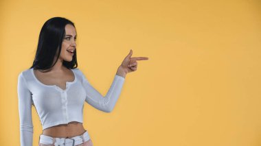 Şaşkın esmer kadın sarıya bakarken parmağıyla işaret ediyor.