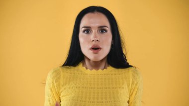 shocked and scared brunette woman looking at camera isolated on yellow clipart