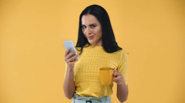 Akıllı telefondan mesaj atan sinsi bir kadın. Elinde sarı çay fincanı tutarken.
